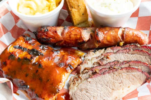 BBQ sampler close-up with sauced ribs, smoked sausage, sliced brisket, mac and cheese, and coleslaw