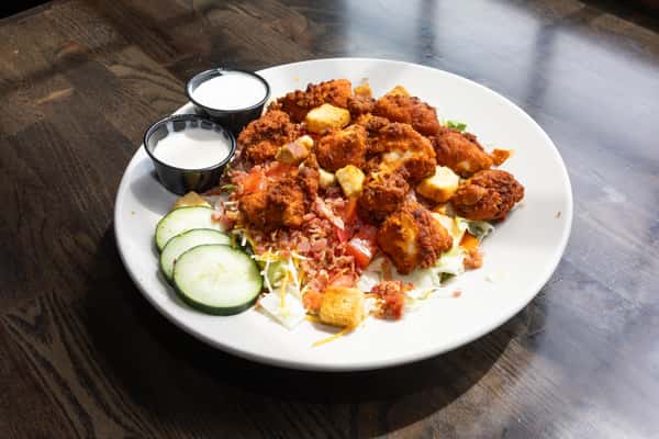 Buffalo chicken salad with crispy fried chicken, bacon, shredded cheese, tomatoes, cucumbers, and ranch dressing on a white plate