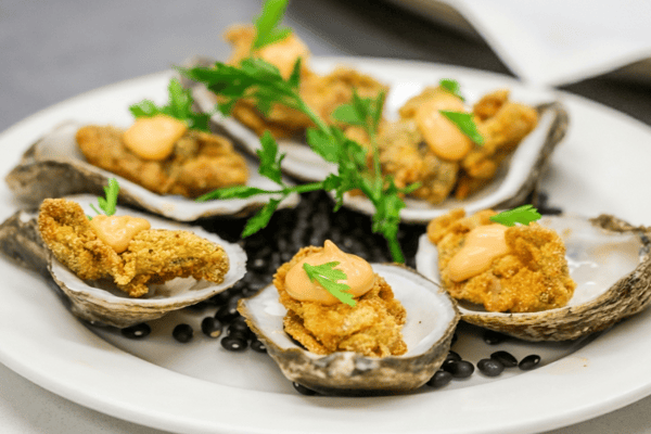 Fried oysters in shells, topped with orange sauce and green parsley, on a white plate with black beans.
