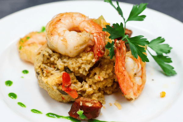 Jambalaya with shrimp, sausage, red peppers, and parsley, garnished with green sauce on a white plate.