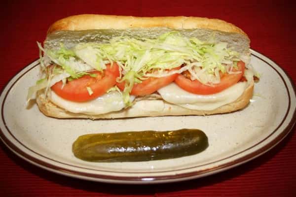 turkey sub with lettuce and tomato. a pickle is on the side