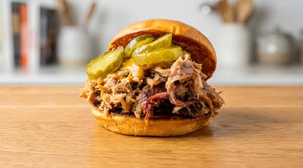 Pulled pork sandwich on a bun with pickles and mustard, on a wooden board.