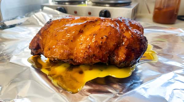 Hickory smoked ham with a sticky glaze, resting on aluminum foil with melted cheese and sauce beneath.