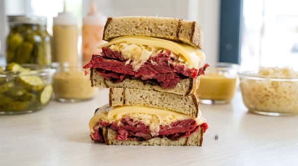 Pastrami Reuben sandwich, cut in half, with cheese, sauerkraut, and rye bread on foil.