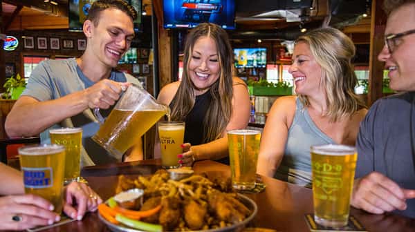 Patrons attending a watch party for a Fantasy Football Leagues gathered around a table enjoying beers and appetizers