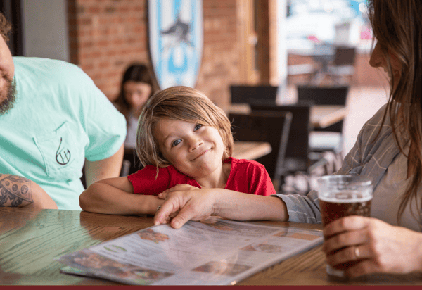 Kid smiling at a dining table sitting between their parents.