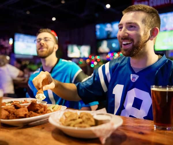 Two men enjoying appetizers and classic American food while watching a game