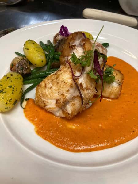 Pan-seared fish atop a roasted red pepper sauce, served with parsley potatoes, green beans, mushrooms, and microgreens.