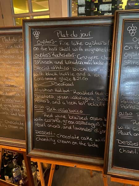 Framed chalkboard menu listing the day's specials, including oysters, duck liver mousse, halibut, pork osso bucco, and chocolate cake.