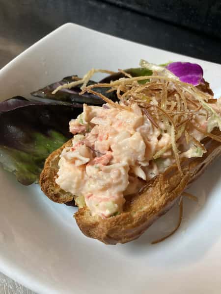 Lobster salad served in a crispy éclair shell with mixed greens and crispy potato garnish.