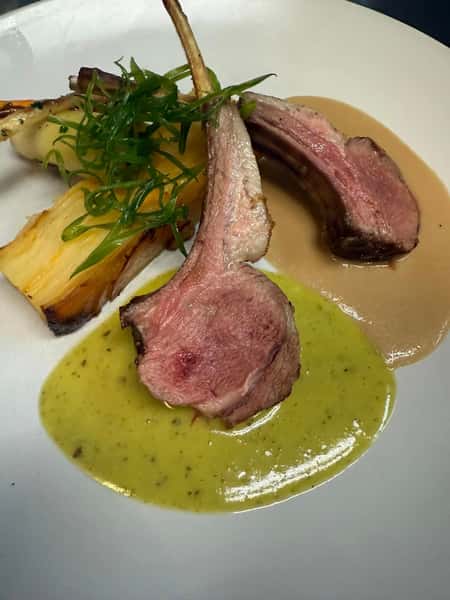 Medium-rare lamb chops plated with golden potato gratin, grilled root vegetables, and duo of green and brown sauces.