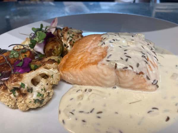 Pan-seared salmon with wild rice cream sauce, served with roasted cauliflower, Brussels sprouts, and microgreens.