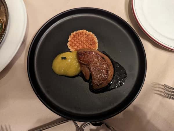 Seared foie gras served with a crisp waffle wafer and a dollop of smooth apple purée on a matte black plate.