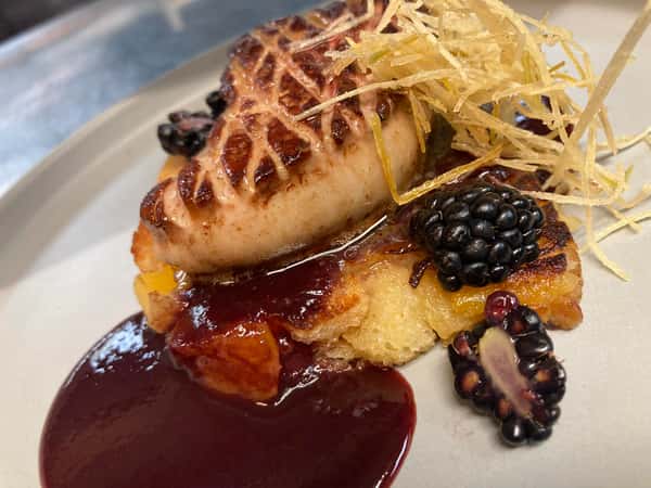 Seared foie gras atop brioche with berry reduction, blackberries, and crispy leeks, elegantly plated for fine dining.