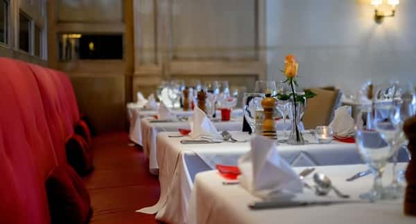 Elegant restaurant interior with white tablecloths, red cushioned seating, folded napkins, and a single yellow rose centerpiece.
