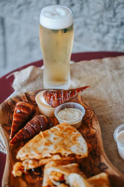 Pub-style appetizer board with pretzel bites, fried green tomatoes, quesadillas, dipping sauces, and draft beer.