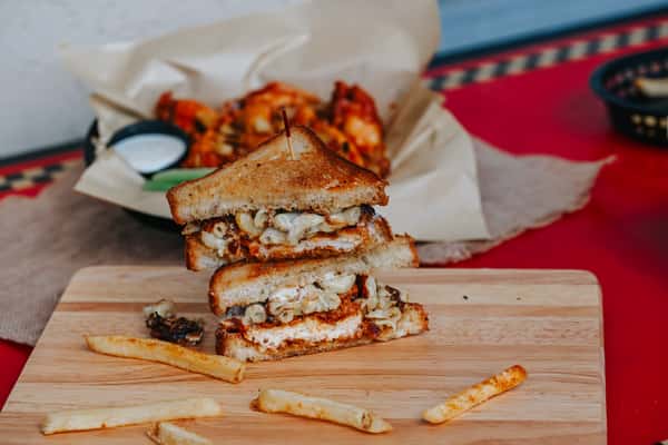 Buffalo chicken sandwich layered with creamy mac and cheese on toasted bread, served with crispy wings and dipping sauce.