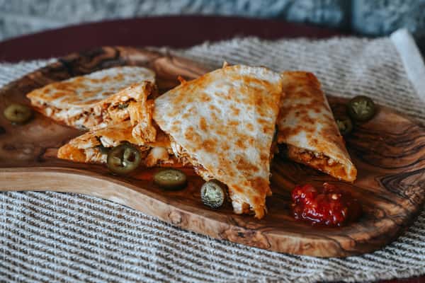 Grilled chicken quesadilla wedges filled with melted cheese and seasoned chicken, served with jalapeños and salsa.