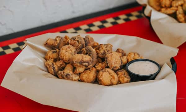 Golden fried mushrooms served with creamy dipping sauce, a crispy appetizer perfect for sharing.