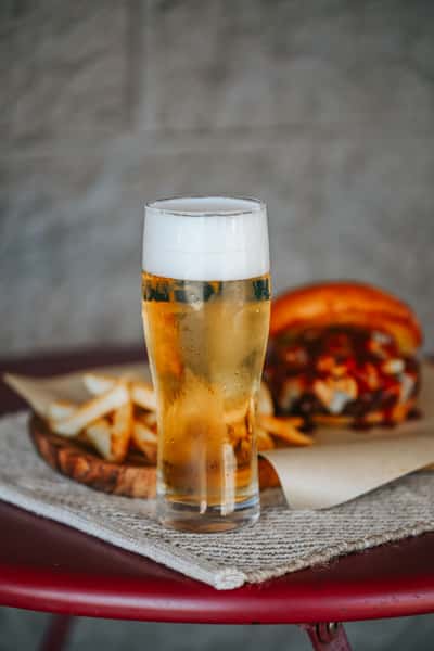 Ice-cold draft beer served in a frosty pint glass alongside burgers and fries in a casual sports bar setting.