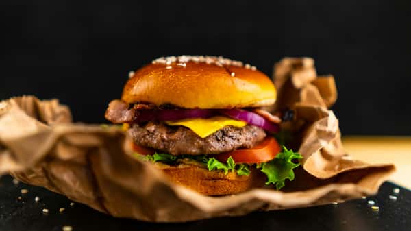Classic cheeseburger with a beef patty, cheddar cheese, crispy bacon, red onions, lettuce, and tomato on a toasted sesame seed bun.