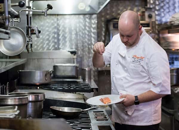 Orange Hill chef sprinkling herbs over a piece of fresh salmon
