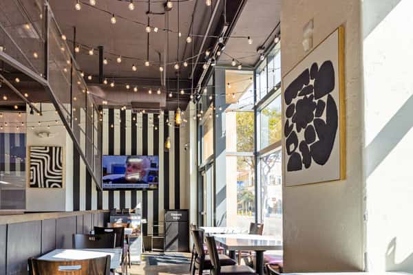 Bright pizza shop dining area with large windows, string lights, and minimalist tables creating a casual modern atmosphere
