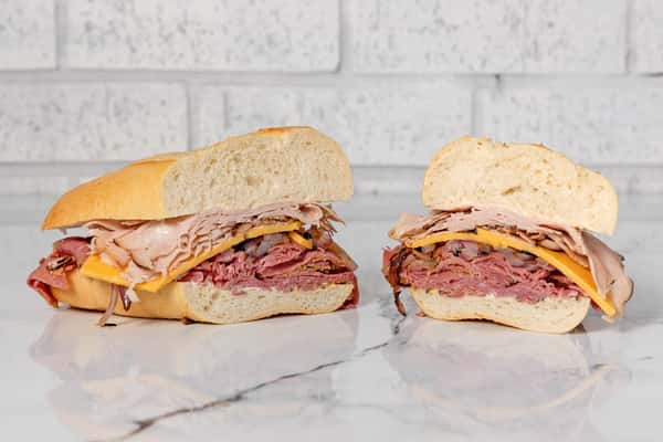 Hot deli sandwich with pastrami, turkey, melted cheese, and grilled onions on a toasted hoagie roll
