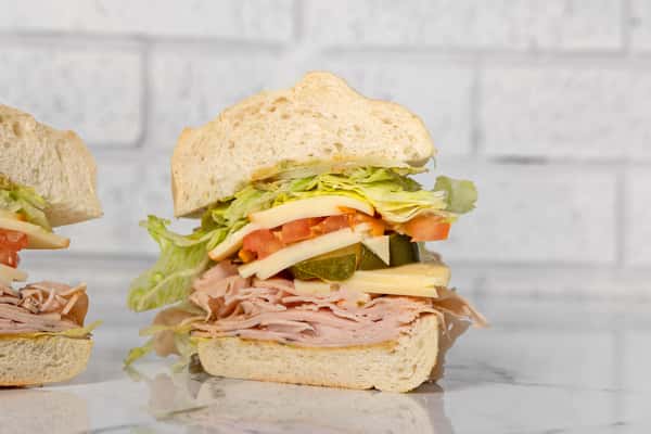 turkey and cheese deli sandwich with lettuce, tomato, pickles, and onions on a soft white roll