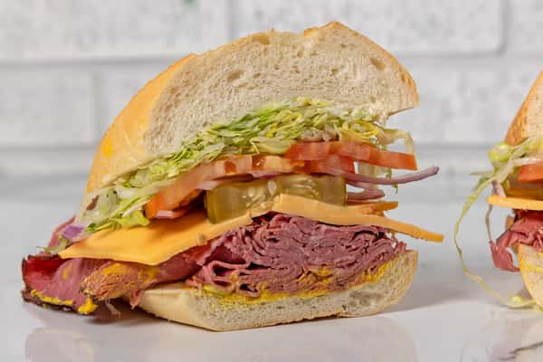 Classic pastrami sandwich with melted cheese, lettuce, tomato, pickles, and onions on a soft roll