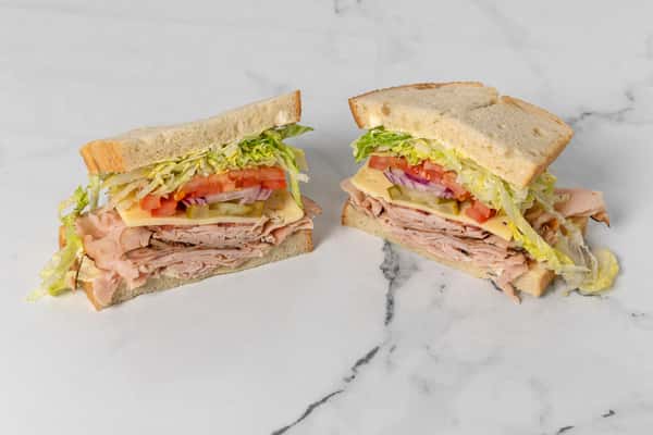 turkey club style sandwich with sliced meat, cheese, lettuce, tomato, and pickles on white bread