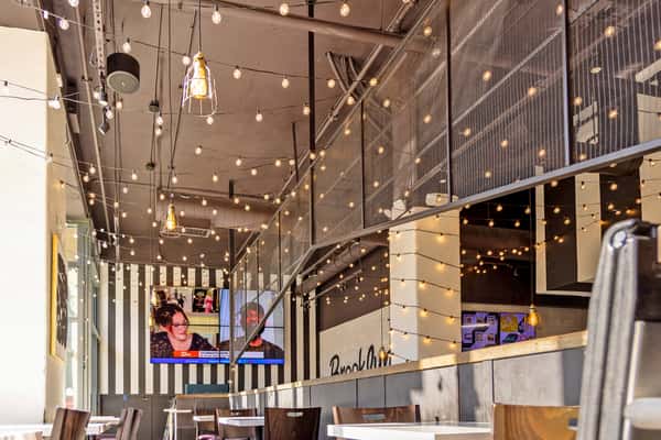Warm modern restaurant interior with string lights, striped accent wall, and casual dining tables at Brooklyn Square