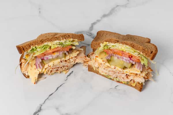 turkey sandwich on wheat bread with cheese, lettuce, tomato, onions, and pickles cut in half