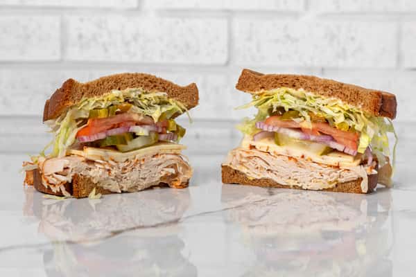 Turkey sandwich on whole grain bread with cheese, lettuce, tomato, pickles, and onions, stacked deli-style
