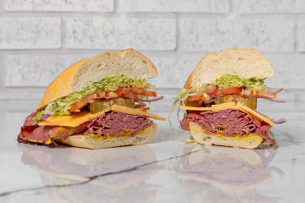roast beef deli sandwich with cheddar cheese, lettuce, tomato, pickles, and onions on a fresh sub roll