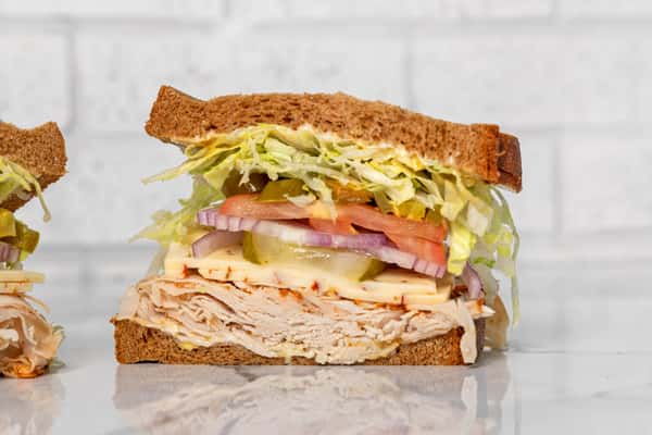 Turkey sandwich on whole grain bread with cheese, lettuce, tomato, pickles, and onions, stacked deli-style