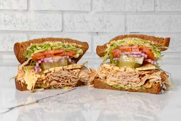 Turkey deli sandwich halves with cheese, lettuce, tomato, pickles, and onions on whole grain bread