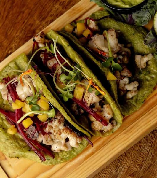 Grilled shrimp tacos served on spinach tortillas, filled with microgreens, julienned beetroot, and mango, paired with guacamole and lime.