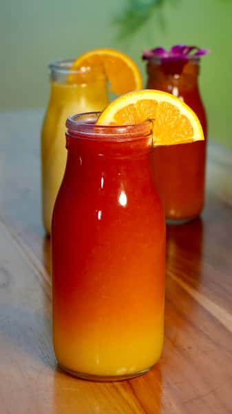 Layered orange and red tropical juice served in a glass bottle, garnished with a fresh orange slice; vibrant and refreshing beverage option.