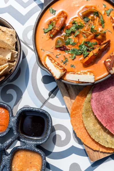 Creamy shrimp stew topped with fresh cilantro and grilled halloumi, served with colorful corn tortillas, house salsas, and tortilla chips—perfect for showcasing modern coastal Mexican cuisine and bold flavors.