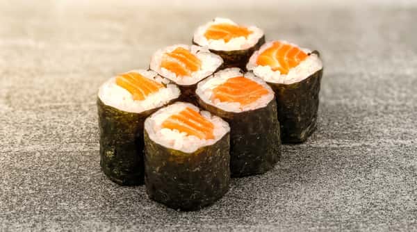 Six salmon maki sushi rolls with bright orange fish, white rice, and dark green nori on a speckled gray surface.