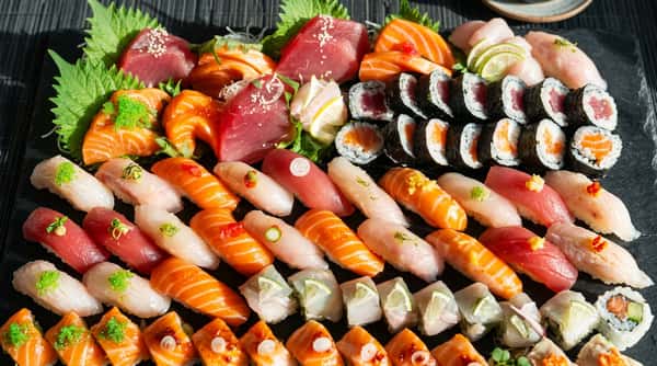 Assorted sushi and sashimi platter with tuna, salmon, and white fish, garnished with lime and herbs.