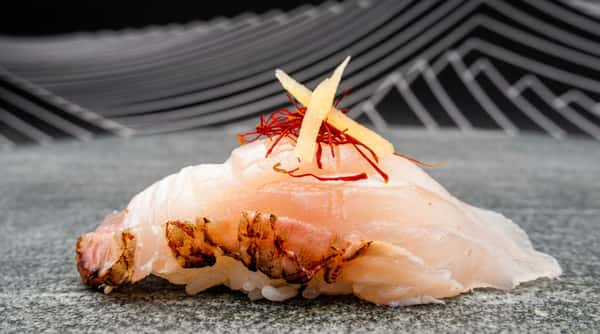 Nigiri sushi with light pink fish, topped with yellow strings of ginger, and red saffron threads.