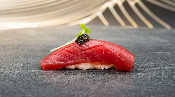 Tuna nigiri sushi with a dark caviar topping and green micro shoots.
