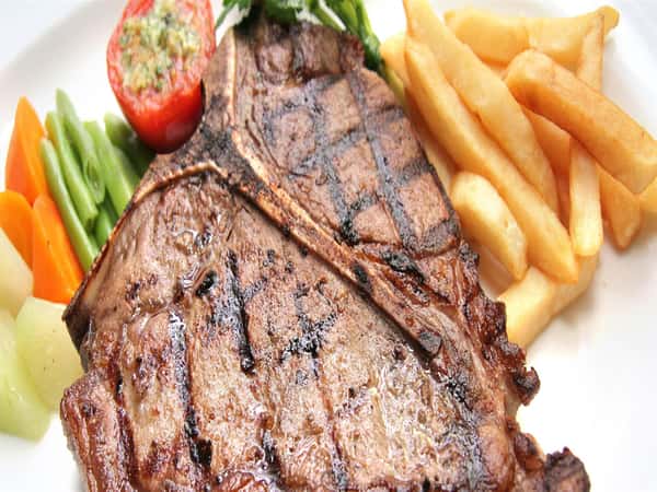 Grilled T-bone steak served with thick-cut golden fries and mixed green and orange vegetables.