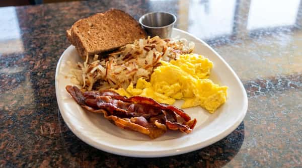 Breakfast plate with scrambled eggs, crispy bacon, hash browns, and a slice of wheat toast.