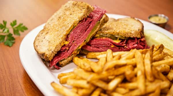 Pastrami sandwich on rye with pickles and mustard, served with a side of french fries.