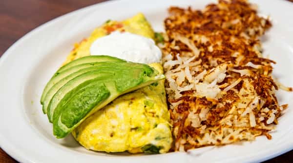 Omelet topped with avocado slices and a dollop of sour cream, served with crispy hash browns.
