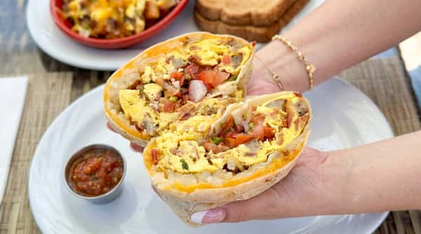 A breakfast burrito cut in half, revealing scrambled eggs, bacon, sausage, diced tomatoes, and onions.