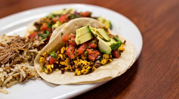 Breakfast tacos with scrambled eggs, pico de gallo, and avocado, served with hash browns.